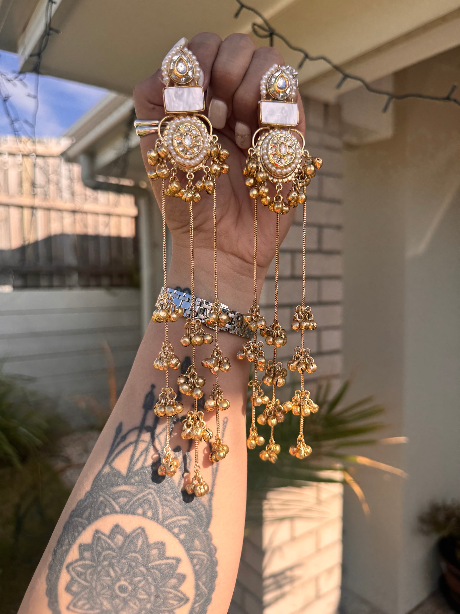 Gold jewelry set held by a hand with a tattoo, outdoor background